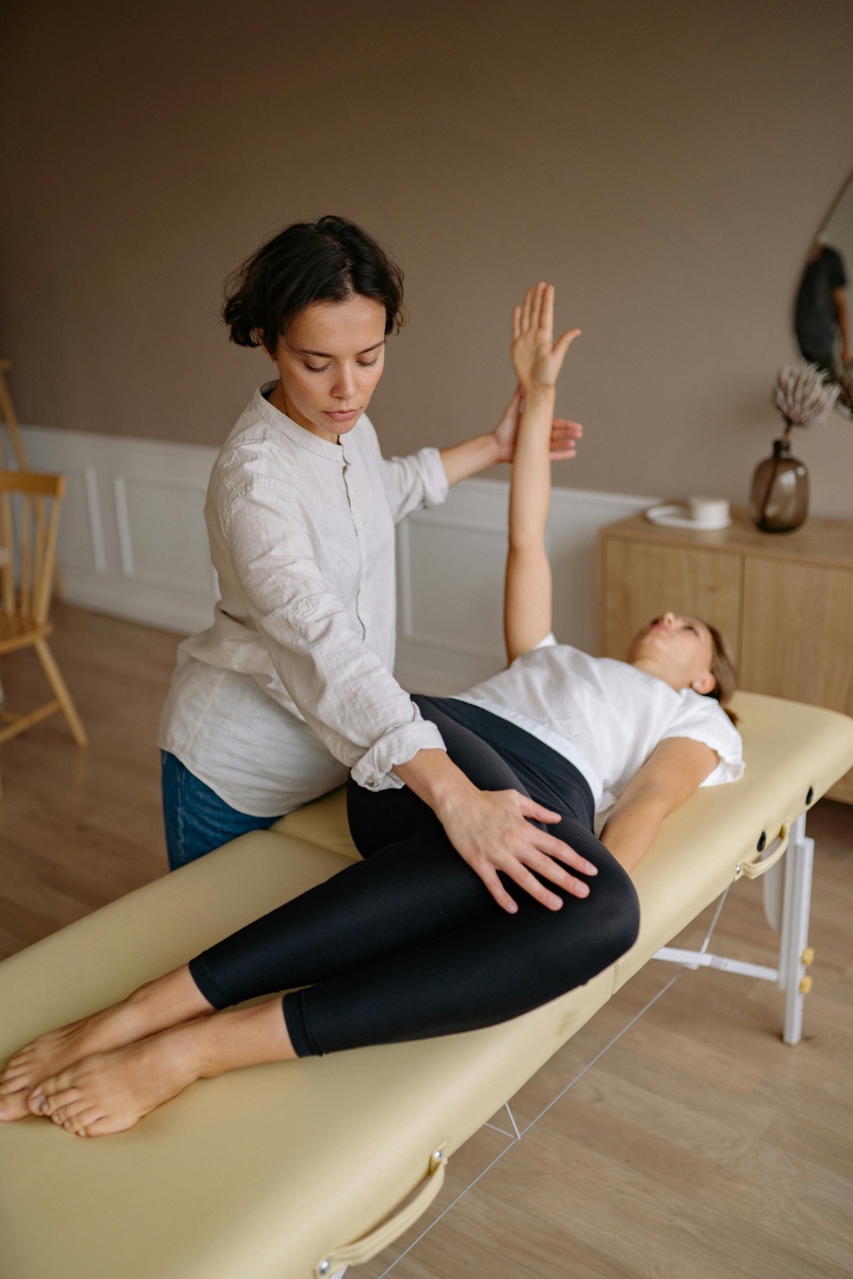 Female physiotherapist guiding a female client through exercises in a treatment room